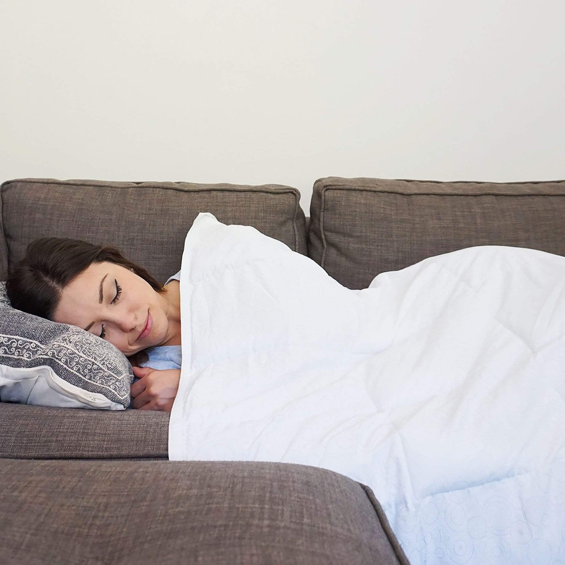 Woman resting beneath a white Coolmax weighted blanket on a sofa