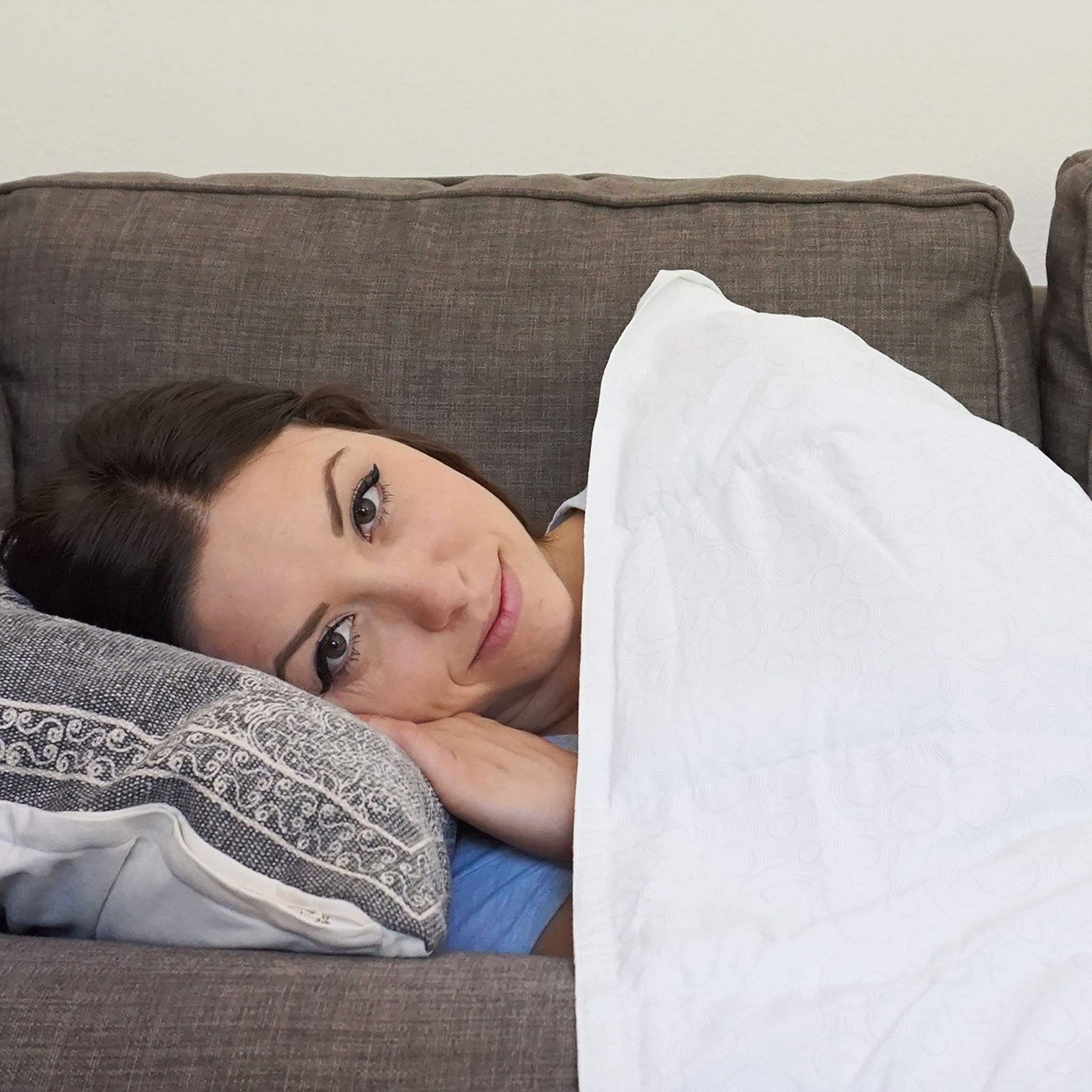 Woman resting on a sofa beneath a white cotton weighted blanket